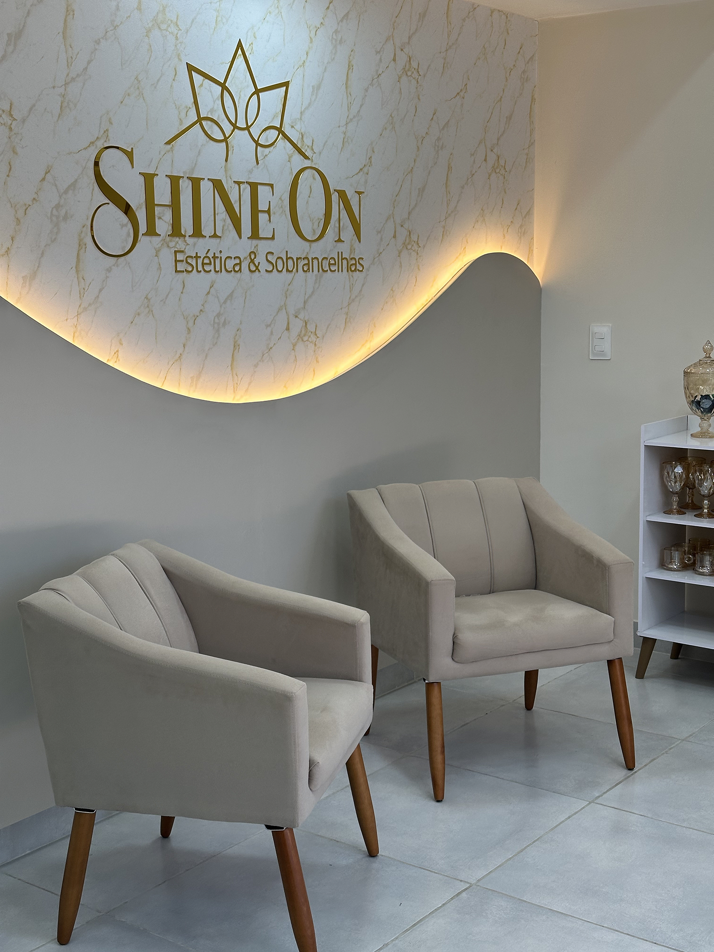 Área de espera do Stúdio Shine com poltronas claras e painel iluminado
